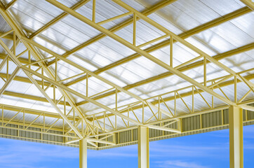 Low angle and perspective side view of yellow metal building roof structure with heat insulations in construction site area with blue sky background