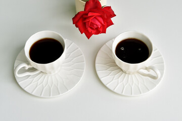 Two cups of coffee and a red rose on a white background