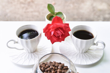 Two cups of coffee, coffee beans and a red rose on a white table