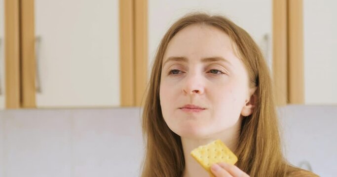 Girl takes bite of cracker and squeezes her eyes shut in pleasure. Young woman eating cookies after diet. Cheat meal.