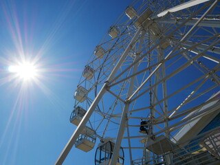 White modern Ferris wheel against the blue sky. Bright rays move away from the sun. Summer walk. 