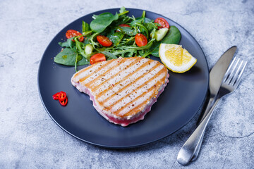 Grilled tuna steak with fresh vegetables, arugula, spinach and lemon. Close-up.