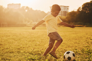Plays soccer. African american kid have fun in the field at summer daytime