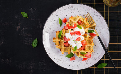 Zucchini waffle, zucchini fritters cooking on waffle maker, vegetarian zucchini waffles with tomatoes, sour cream and basil  in a white plate. Top view, flat lay