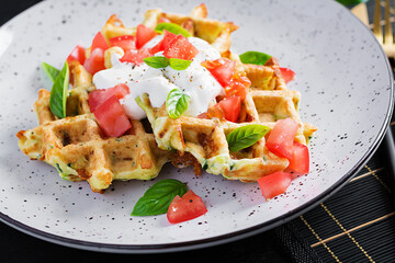 Zucchini waffle, zucchini fritters cooking on waffle maker, vegetarian zucchini waffles with tomatoes, sour cream and basil  in a white plate.