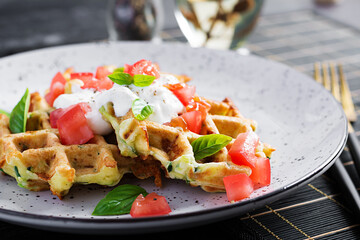 Zucchini waffle, zucchini fritters cooking on waffle maker, vegetarian zucchini waffles with tomatoes, sour cream and basil  in a white plate.