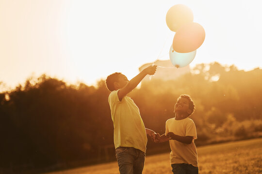 Playing with air balloons. Two african american kids have fun in the field at summer daytime together