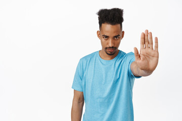 Image of serious angry african american man stretch out hand, tell to stop, furrow eyebrows and...
