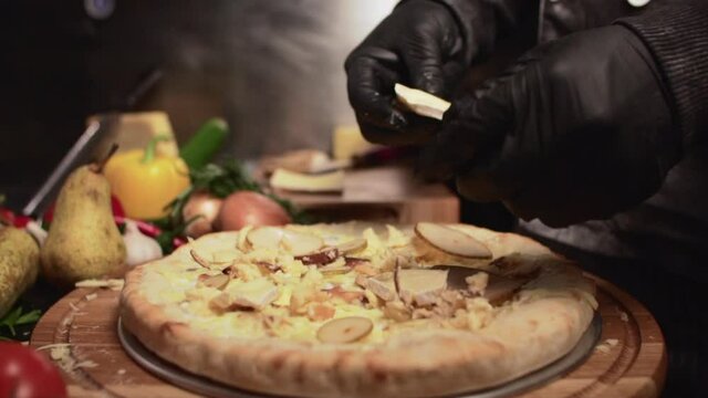 The chef prepares a vegetarian pizza. A man in a black jacket lays out the ingredients on the dough.