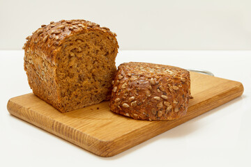 Cut loaf of bread on wooden cutting board on white background