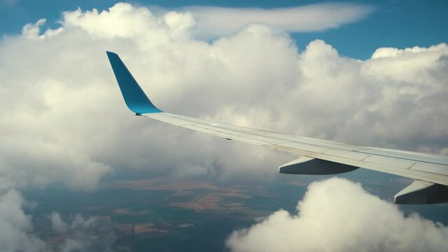 View of jet airplane wing from inside flying through white puffy clouds in blue sky. Travel and air transportation concept.