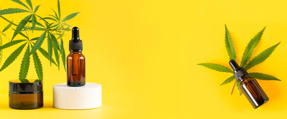 Amber glass cosmetic bottles with CBD oil and hemp leaves stand on the podium. Cosmetics CBD oil on a yellow background. Copy space for text.