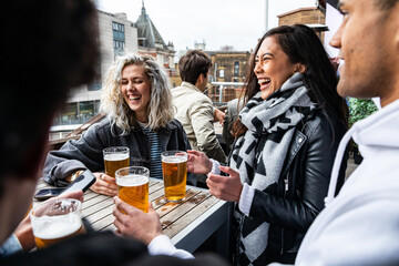People enjoying a beer together at pub brewery - Happy laughing man and women talking and raising pint glass - Lifestyle and drink concepts in London - 444258003