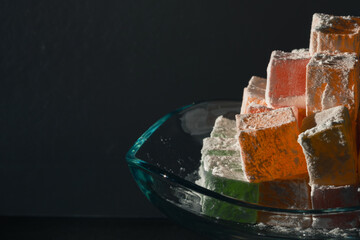 Turkish delights illuminated by sunlight on the glass bowl isolated on black background. Ramazan...