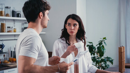man with newspaper looking at seductive woman drinking coffee in kitchen