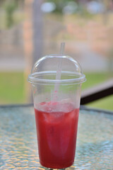 Smoothie cocktail with ice in a plastic cup, closed with a lid with tubes, on a blurry background