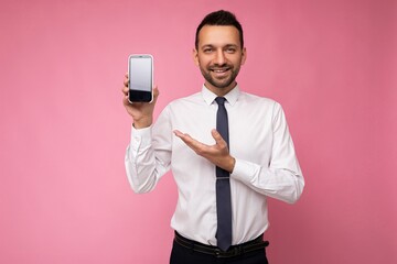 Photo of handsome smiling adult male person good looking wearing casual outfit standing isolated on background with copy space holding smartphone showing phone in hand with empty screen display for