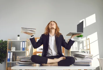 Abwaschbare Fototapete Calm positive barefoot busy office worker in suit breathes deeply and meditates holding papers and laptop and relaxing in lotus yoga pose on desk with document piles. Balance and stress relief at work © Studio Romantic