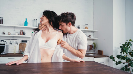 young man undressing seductive woman in white shirt and bra in kitchen