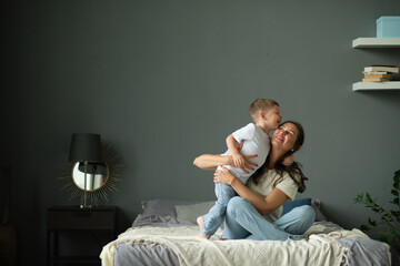 mother hugs with her toddler little son on a bed together. Family moments, children care....