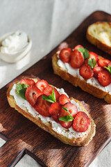 Two toasts or bruschetta with strawberry and cream cheese on wooden board. Summer breakfast