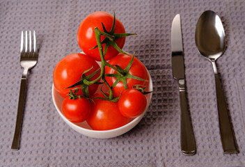 a bunch of red tomatoes in a white plate with a fork and spoon. Red tomatoes on the table.