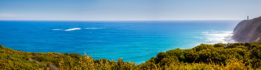 Fototapeta na wymiar Landscape Panorama from the green hills to the horizon line in the blue ocean. Lighthouse on a hill near the sea. Ocean coast with rainforest and lighthouse. Australia.