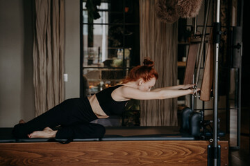 Obraz na płótnie Canvas Flexible ginger woman stretching arms on cadillac reformer