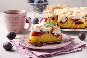 Homemade plum pie covered with sweet meringue on a plate on a light background close-up.