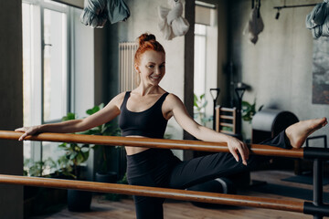 Happy young woman good stretch posing in fitness studio during barre workout