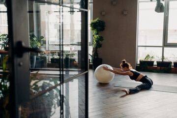 Young woman exercising with fitball, doing stretching exercises in fitness studio