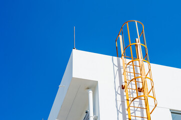 yellow metal ladder to roof (fire escape) on a white wall of building,safety ladder for roof...
