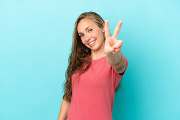 Young caucasian woman isolated on blue background smiling and showing victory sign