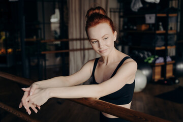 Fototapeta na wymiar Pretty young red haired woman leaning on ballet barre