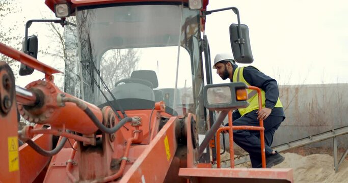 Man in hardhat entering tractor at building site