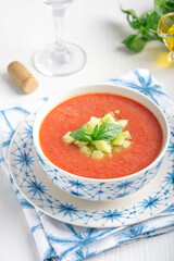 Portion of fresh Andalusian spanish gazpacho cold refreshing tomato soup made of raw blended vegetables eaten during hot summers served in bowl with basil, cucumber cubes and glass of wine. Vertical