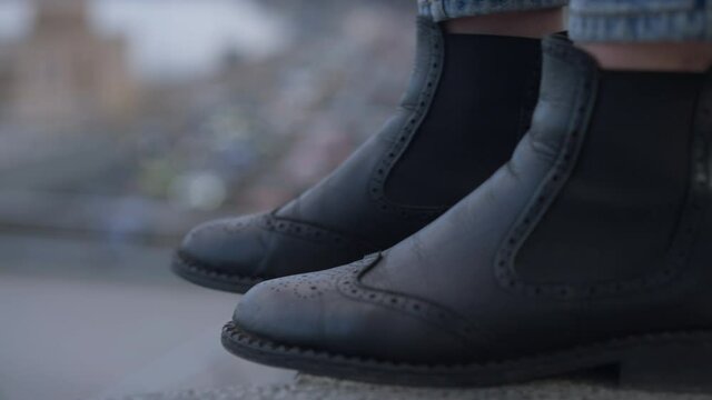 Female Feet In Black Boots On Bridge Edge With Blurred Cars Riding On Road Down. Unrecognizable Depressed Suicidal Young Woman Attempting Suicide In Urban City Outdoors