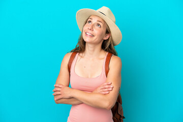 Young caucasian woman in summer holidays isolated on blue background looking up while smiling