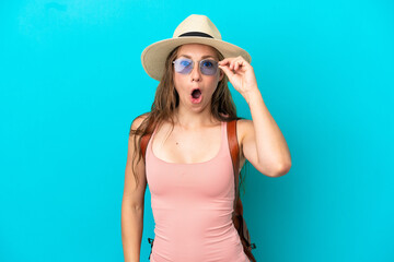 Young caucasian woman in summer holidays isolated on blue background with glasses and surprised