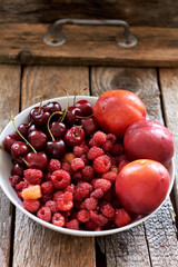 red berries and fruits in a plate on a wooden background
