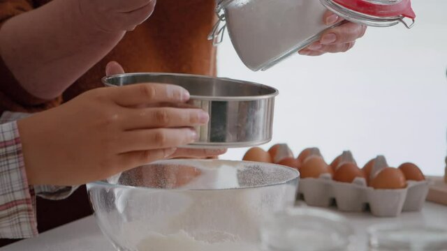 Closeup of grandmother putting flour ingredient in strainer while grandchild preparing traditional winter cookie in culinary kitchen. Family enjoying christmas holidays making homemade dessert