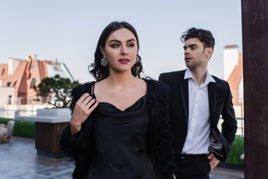 elegant woman in faux fur jacker near man on terrace