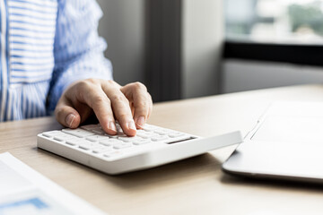 Female auditor pressing white calculator, she is a private company auditor, she is reviewing numbers of company financial statements before presenting them to senior management. Audit concept.