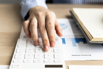Female auditor pressing white calculator, she is a private company auditor, she is reviewing numbers of company financial statements before presenting them to senior management. Audit concept.