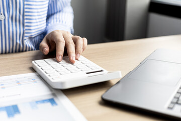 Fototapeta premium Female auditor pressing white calculator, she is a private company auditor, she is reviewing numbers of company financial statements before presenting them to senior management. Audit concept.