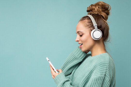 Side-ptofile closeup photo of beautiful young woman wearing stylish casual outfit isolated over colorful background wall wearing white wireless headphones and listening to music and using mobile phone