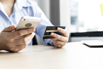 A woman holding a cell phone and credit card, she fills in her credit card information in a mobile shopping app to pay for the purchase. Online shopping concept using credit card payments.