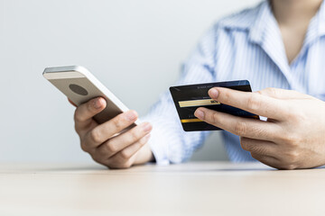A woman holding a cell phone and credit card, she fills in her credit card information in a mobile shopping app to pay for the purchase. Online shopping concept using credit card payments.