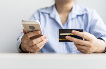 A woman holding a cell phone and credit card, she fills in her credit card information in a mobile shopping app to pay for the purchase. Online shopping concept using credit card payments.