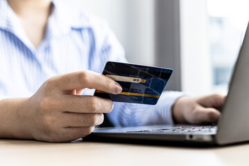 Woman typing on a laptop keyboard and holding a credit card, she fills in her credit card information on a laptop shopping app to pay for the order. Online shopping concept using credit card payments.